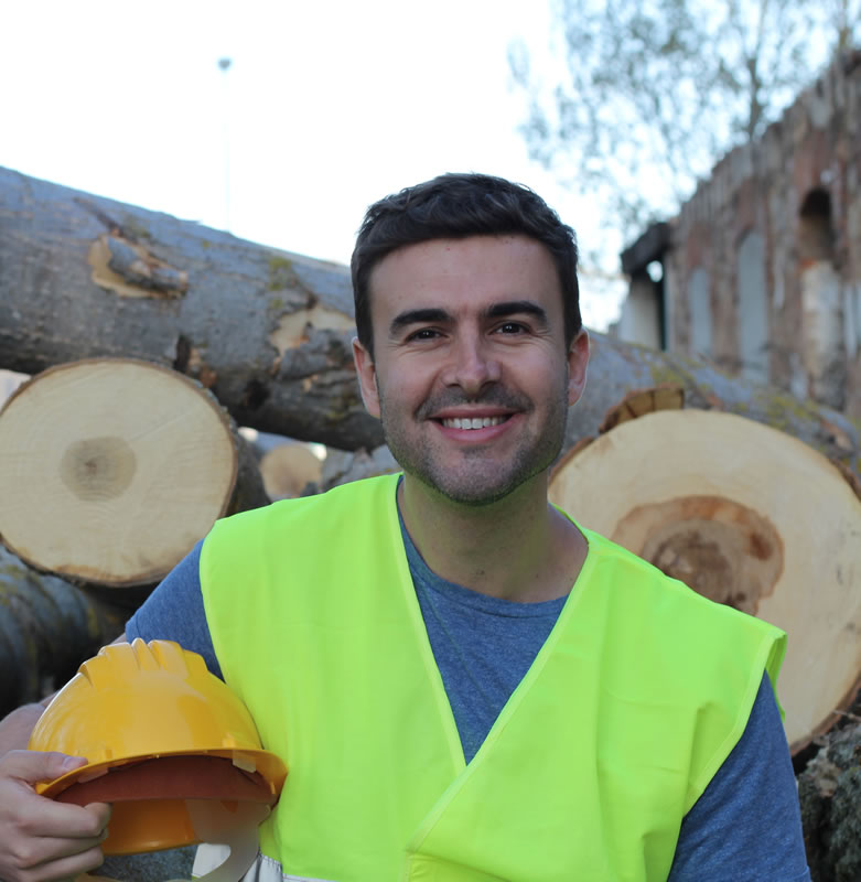 Tree surgeon standing infront of logs holding hard hat